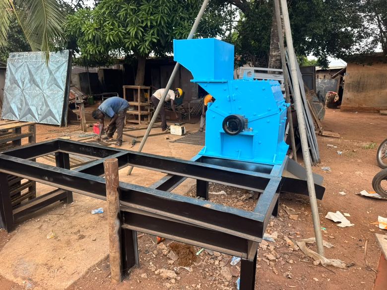 Machine bleue à trémie montée sur un châssis noir, dans un atelier à ciel ouvert